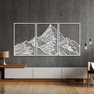 May include: A white metal wall art sculpture depicting a mountain range with a minimalist line art design. The sculpture is divided into three panels and is mounted on a gray wall above a wooden entertainment center.