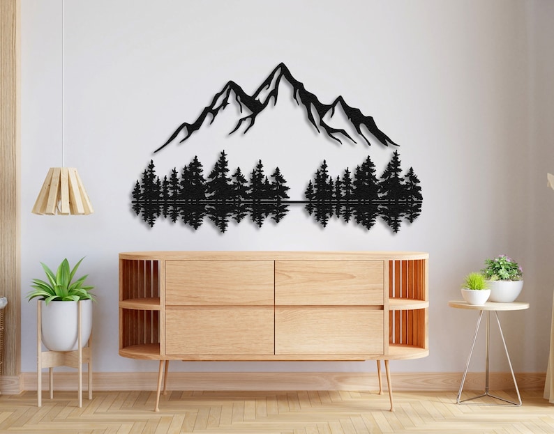 May include: Black metal wall art depicting a mountain range with a reflection of trees in a lake. The art is mounted on a white wall above a wooden dresser.
