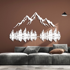 May include: White silhouette wall art depicting a mountain range with trees reflected in a lake. The art is mounted on a brown wall above a gray couch.