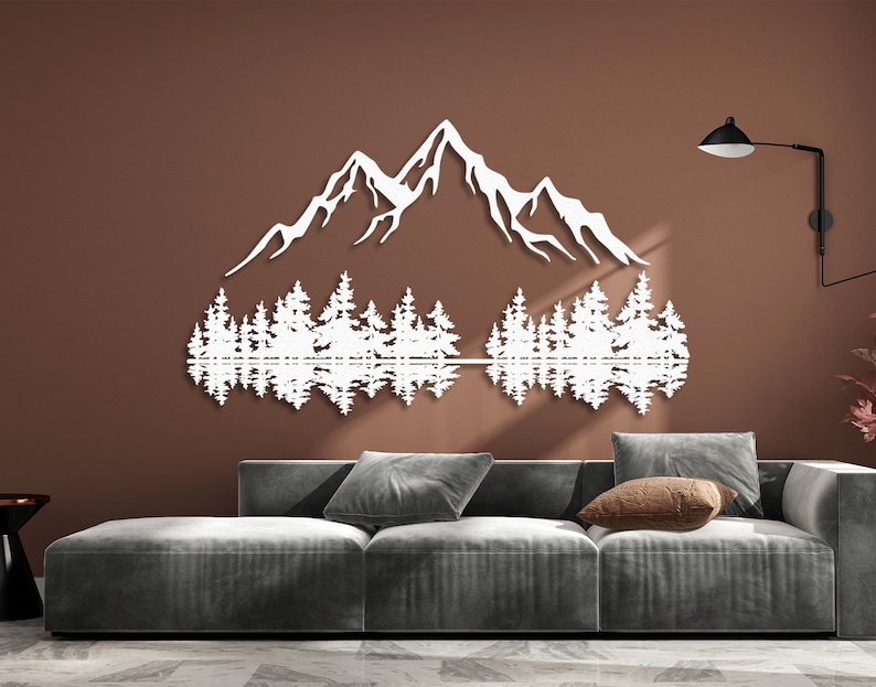 May include: White silhouette wall art depicting a mountain range with trees reflected in a lake. The art is mounted on a brown wall above a gray couch.