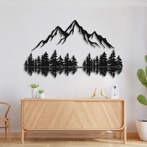 May include: Black metal wall art depicting a mountain range with a reflection of the mountains in a lake below. The mountains are silhouetted against a white background. The art is mounted on a white wall above a wooden dresser.