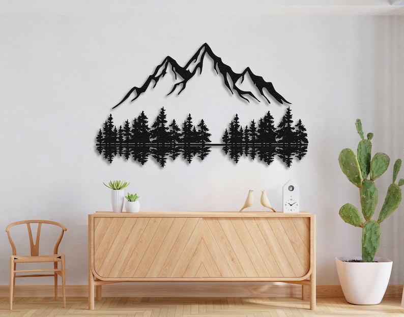 May include: Black metal wall art depicting a mountain range with a reflection of the mountains in a lake below. The mountains are silhouetted against a white background. The art is mounted on a white wall above a wooden dresser.