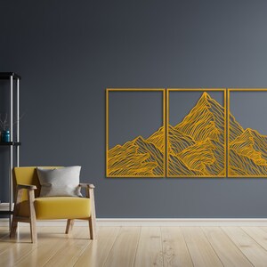 May include: A three-piece wall art set featuring a stylized mountain range design in a gold color. The design is made up of thin lines that create a textured effect. The wall art is mounted on a dark gray wall.