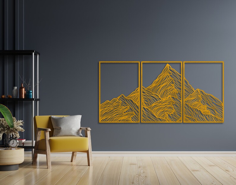 May include: A three-piece wall art set featuring a stylized mountain range design in a gold color. The design is made up of thin lines that create a textured effect. The wall art is mounted on a dark gray wall.
