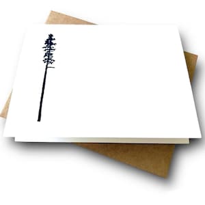 May include: A blank white card with a black silhouette of a pine tree in the upper left corner. The card is folded in half and has a brown envelope behind it.