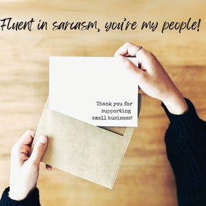 Puede incluir: Una tarjeta rectangular blanca dentro de un sobre color canela. La tarjeta tiene el texto impreso en negro: Thank you for supporting small business! Arriba, el texto negro dice: Fluent in sarcasm, you're my people! La tarjeta est&aacute; sujeta.
