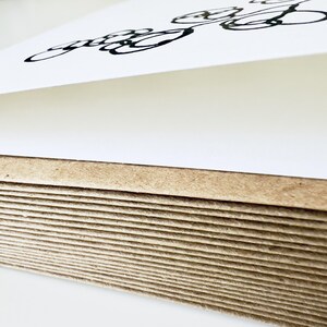 May include: A stack of thick, rectangular paper sheets with a natural brown, fibrous edge. The top sheet is white and features a black, hand-drawn ink illustration consisting of several overlapping circular loops and curved lines.