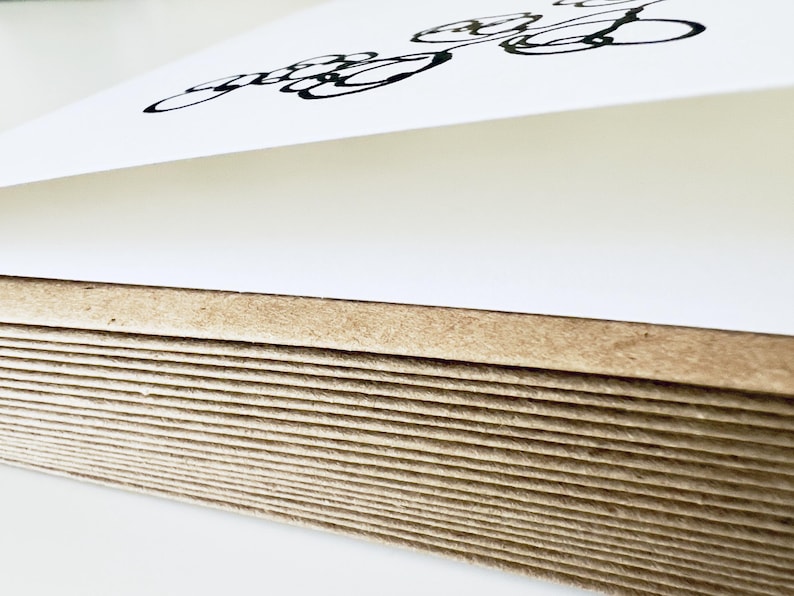 May include: A stack of thick, rectangular paper sheets with a natural brown, fibrous edge. The top sheet is white and features a black, hand-drawn ink illustration consisting of several overlapping circular loops and curved lines.