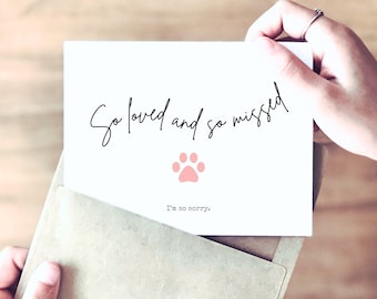 May include: A white rectangular sympathy card featuring the black cursive text So loved and so missed, a small light pink paw print icon, and the black typewriter-style text I'm so sorry, partially inserted into a tan paper envelope.
