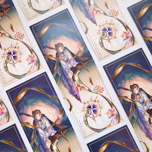 May include: A set of bookmarks featuring a colourful illustration of a person in a flowing robe with gold ribbons and a star-shaped design. The bookmarks have a dark background and a light beige border.