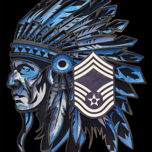 May include: A layered wooden art piece featuring a Native American chief in profile, adorned with a feathered headdress. The design incorporates shades of blue, black, and silver, with a military insignia on the right side. The background is black.
