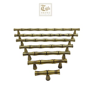 Può includere: Un set di otto maniglie per armadi in stile bambù color oro. Le maniglie sono disposte in uno schema sfalsato, con la maniglia più piccola in basso e la più grande in alto. Tutte le maniglie sono in metallo e hanno una finitura liscia e lucida.