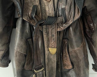 May include: A brown leather trench coat with a black belt and a brown leather lining. The coat has a button closure and a collar.