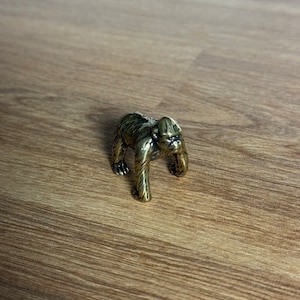 Op de afbeelding: Een klein, goudkleurig beeldje van een gorilla. De gorilla staat op alle vier poten en heeft een gedetailleerd gezicht.