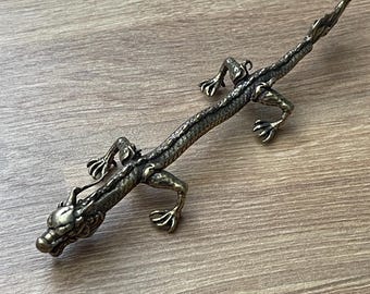 May include: A detailed bronze dragon figurine with intricate scales, claws, and a detailed head. The dragon is posed on a wooden surface, showcasing its detailed craftsmanship. The figurine is a decorative item.