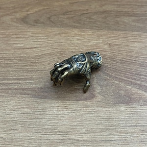 Könnte beinhalten: Eine detaillierte Bronzeskulptur einer Hand, mit bandagierten Fingern. Die Hand ist so positioniert, als würde sie nach etwas greifen.