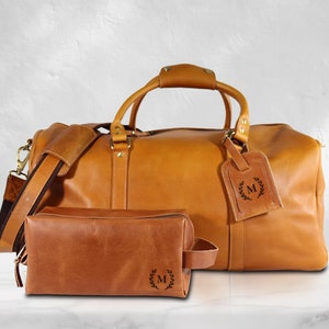 May include: A brown leather travel duffel bag with a matching brown leather toiletry bag. Both bags have a monogrammed "M" with a laurel wreath design.