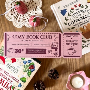 Peut inclure: Un billet rose et marron avec le texte "Cozy Book Club" et "Venez comme vous êtes avec votre meilleur livre douillet". Le billet comprend également une petite illustration d'un ours en peluche portant une écharpe. Le billet coûte 30 centimes.
