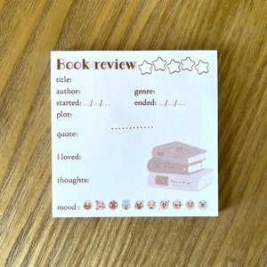May include: A white book review template with a stack of three books, five stars, and a row of emojis. The template has fields for title, author, genre, started, ended, plot, quote, I loved, thoughts, and mood.