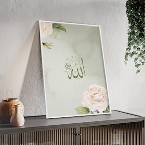 Op de afbeelding: Een ingelijst afdruk met een groene achtergrond en witte bloemen. Het Arabische woord "Allah" is in groene kalligrafie in het midden van de afdruk geschreven.