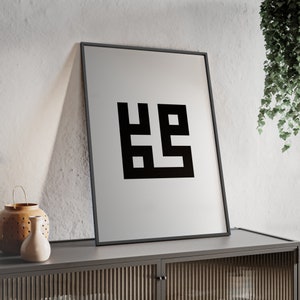Op de afbeelding: Een zwart-wit geometrisch ontwerp print in een zwart frame dat aan een muur hangt boven een houten kast.