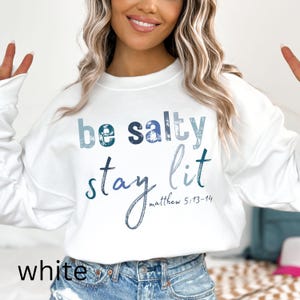 May include: White sweatshirt with a blue and white graphic that says "be salty stay lit" with the scripture reference "matthew 5:13-14" underneath.