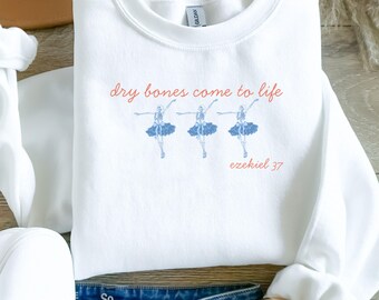 May include: White sweatshirt with the text "dry bones come to life" in red script above three blue skeleton ballerinas. The text "ezekiel 37" is below the ballerinas. The sweatshirt is a crew neck.