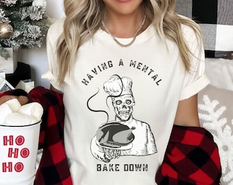 May include: White t-shirt with a black and white illustration of a skeleton chef holding a turkey. The text "Having a mental bake down" is printed on the shirt.