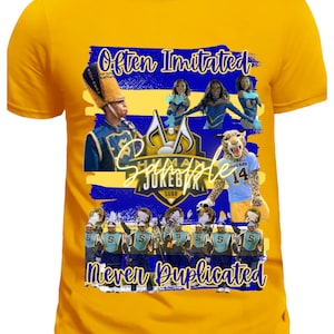 May include: A yellow t-shirt with a blue and gold design. The design features a marching band, cheerleaders, and a mascot. The text "Often Imitated Never Duplicated" is printed on the shirt. The text "Human Jukebox" is also printed on the shirt.