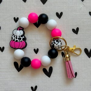 Llavero de muñeca con estampado de vaca rosa, negro y blanco, calabaza, cuentas de silicona y cierre de mosquetón.