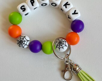 Llavero elástico de cuentas de silicona en naranja, verde y morado con forma de telaraña y letras.