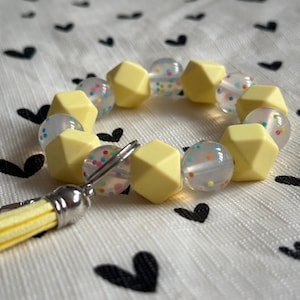 Llavero de pulsera con cuentas de silicona amarillas y confeti y cierre de mosquetón.