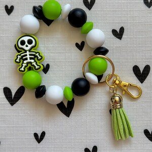 Llavero de pulsera con esqueleto de silicona verde, blanco y negro y cierre de mosquetón.