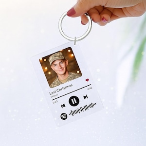 May include: A clear acrylic keyring with a silver ring. The keyring features a photo of a person in a military uniform, with the text "Last Christmas" and a music player interface design. A small red heart is visible.