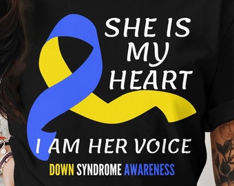 May include: Black t-shirt with a blue and yellow ribbon design. The text reads "SHE IS MY HEART I AM HER VOICE DOWN SYNDROME AWARENESS" in white and blue. The shirt is a crew neck.