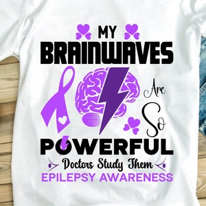 May include: White t-shirt with purple and black text that reads "My brainwaves are so powerful, Doctors study them. Epilepsy Awareness". The text is surrounded by purple hearts and a purple ribbon.