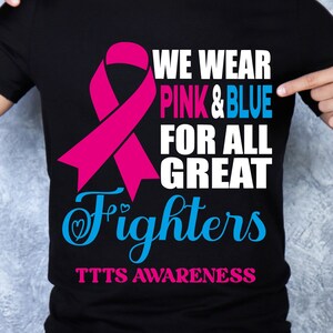 以下が含まれることがあります： ピンクのリボンと「We wear pink & blue for all great fighters TTTS awareness」というテキストが書かれた黒いTシャツ。