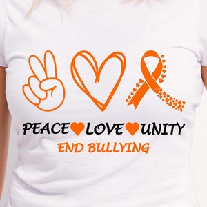May include: White t-shirt with an orange peace sign, heart, and ribbon with the text "Peace Love Unity End Bullying".