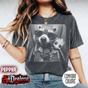 May include: A charcoal Comfort Colors t-shirt with a black and white graphic of Rocket Raccoon in sunglasses and Baby Groot. The shirt has the text "AdDealova" and "Pepper" printed on it.