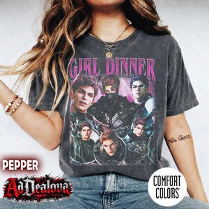 Può includere: Una t-shirt a maniche corte grigio antracite con una stampa grafica di cinque personaggi maschili dai capelli scuri e il testo rosa GIRL DINNER. La maglietta ha un aspetto vintage slavato con scollo rotondo e un design dalla vestibilità ampia.