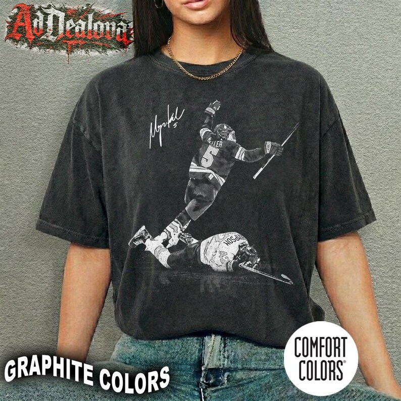 May include: Graphite-colored t-shirt featuring a black and white image of a hockey player in action, with a signature and the text "Graphite Colors". The shirt is from Comfort Colors.