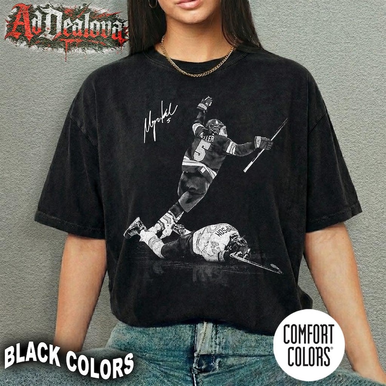 May include: Black Comfort Colors t-shirt featuring a black and white image of a hockey player in action, with a signature and the number 5. The shirt also has the text "BLACK COLORS" and "COMFORT COLORS".