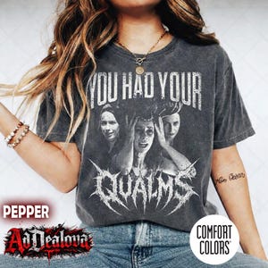 May include: A charcoal gray short-sleeve t-shirt featuring a distressed white graphic print. The design displays three black and white portraits of individuals with the text YOU HAD YOUR QUALMS printed in a bold, stylized, and jagged font.