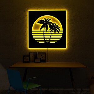 May include: A backlit wall art piece featuring a black silhouette of palm trees and a setting sun design. The artwork is illuminated with a warm yellow glow, creating a tropical aesthetic. The piece is square and mounted on a wall.