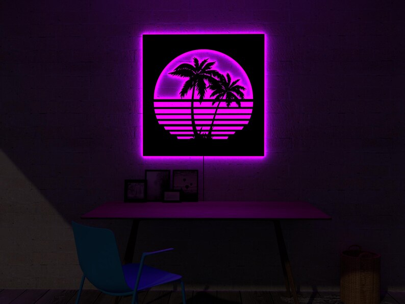May include: A square, black wall art piece with a neon pink border and a retro sunset design. The design features palm trees, a sun, and horizontal lines. The art is mounted above a desk with a blue chair.