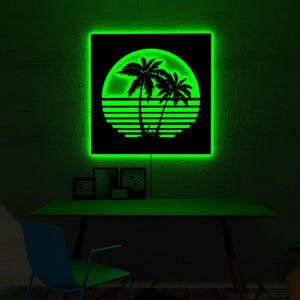 May include: A neon green backlit wall art piece featuring a black silhouette of palm trees against a sunset design. The artwork is square and mounted on a dark wall. A desk and chair are below the artwork.