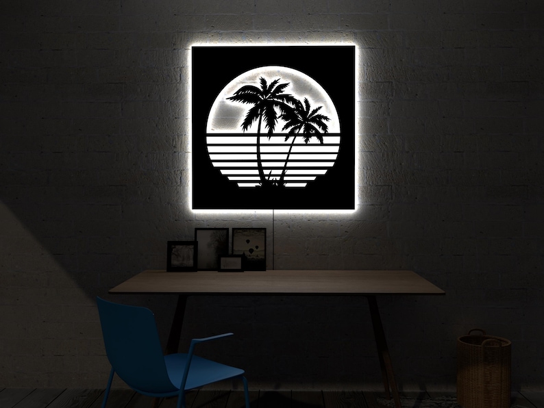 May include: A black and white illuminated wall art piece featuring a tropical sunset scene with palm trees and a setting sun. The artwork is square and has a bright white border. The art is displayed above a wooden desk.