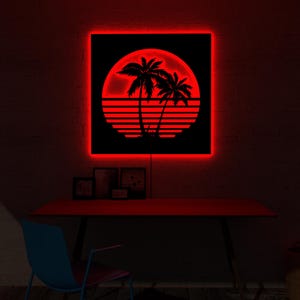 May include: A red neon sign with a black square featuring a tropical sunset scene with palm trees. The sign is mounted on a dark brick wall above a red desk. The room is dimly lit.