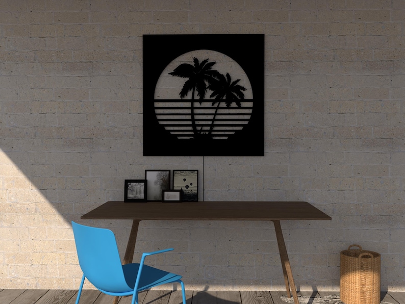 May include: Black metal wall art featuring a tropical sunset scene with palm trees and a sun. The artwork is mounted above a wooden desk with a blue chair. Several framed photos are on the desk, and a woven basket sits nearby.