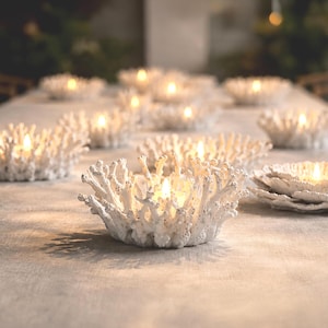 May include: A collection of white, textured candle holders shaped like branching coral. Each bowl-like vessel features intricate, organic protrusions and holds a small, glowing light, creating a warm, illuminated display across the surface.